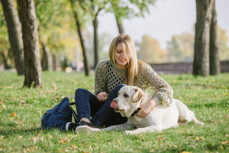 美丽的金发女郎坐在草地上的公园和她的狗拉布拉多