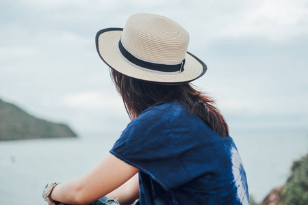 旅行的年轻女子在休闲礼服与帽子独自坐在海滩有海背景