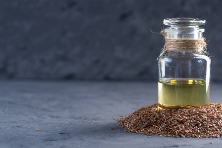 亚麻籽在一堆和亚麻籽的金油在玻璃瓶在桌子上的黑暗背景。健康饮食与欧米茄3脂肪酸的概念