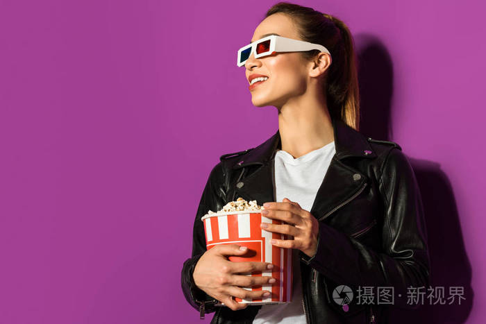 美丽的微笑亚洲女孩在3d 眼镜拿着爆米花, 看着远离紫色的孤立