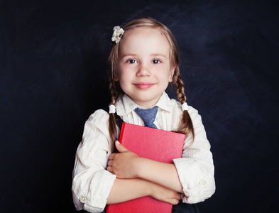 微笑的女学生与书在蓝色粉笔板背景。快乐的孩子肖像。回到学校和教育理念