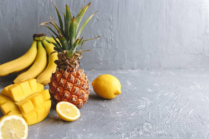 黄色的水果。成熟的多汁菠萝与芒果, 香蕉和柠檬在灰色的木桌上。复制空间