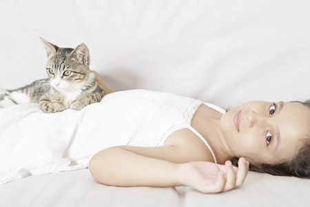 年轻的女孩和猫咪躺在白色的沙发