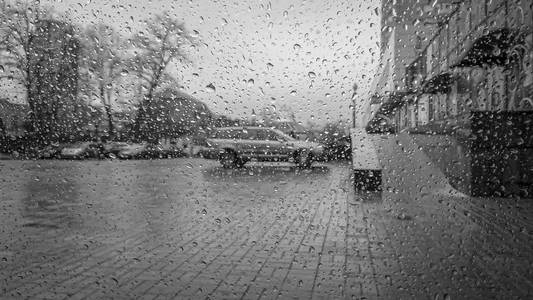城市景观在雨天通过玻璃与水滴的水。黑色和白色城市街道背景