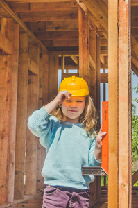 一个孩子, 一个戴着头盔的女孩, 手里拿着一个角落的木制框架房子。