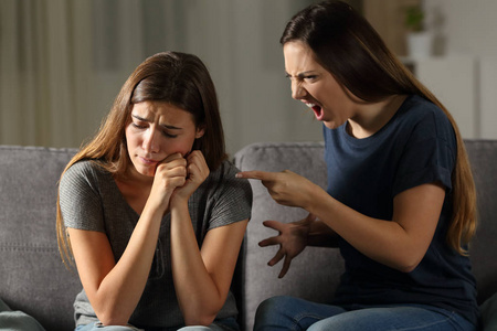 愤怒的女人责骂她的悲伤的朋友坐在沙发上的客厅在家里