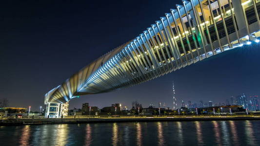 未来的扭曲的行人桥在迪拜运河照亮了夜间 timelapse hyperlapse, 阿联酋。背景景观。从长廊查看