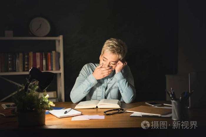 疲惫的学生女孩读书在黑暗的房间