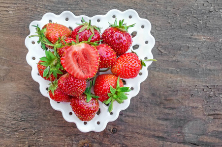 成熟多汁的红色草莓, 在一个白色的盘子上的形状在一个模糊的背景心脏