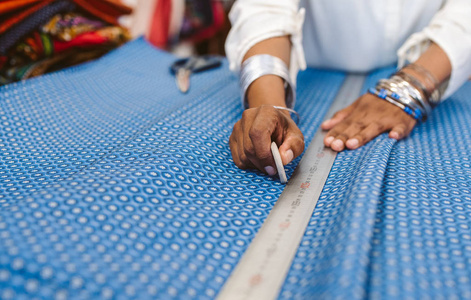 特写的织物店老板站在柜台测量和标记一块漂亮的布料前切割