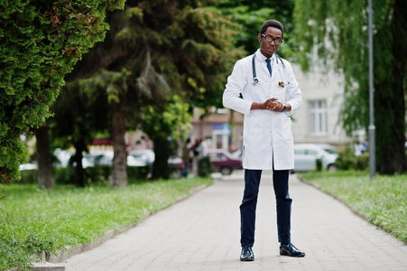 时尚的非洲裔美国医生与听诊器和实验室大衣, 在眼镜摆在室外