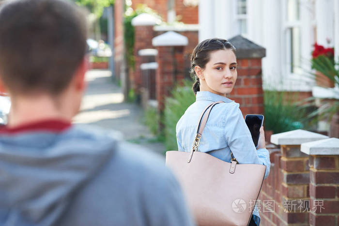在城市街道上被跟踪的年轻妇女在手机上发短信求助照片-正版商用图片