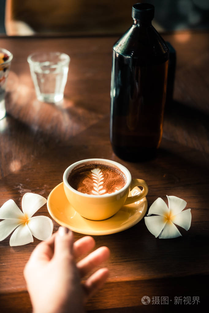 女人的手拿着咖啡在黄色杯子里用铁艺画时髦咖啡店的木桌复古色滤镜