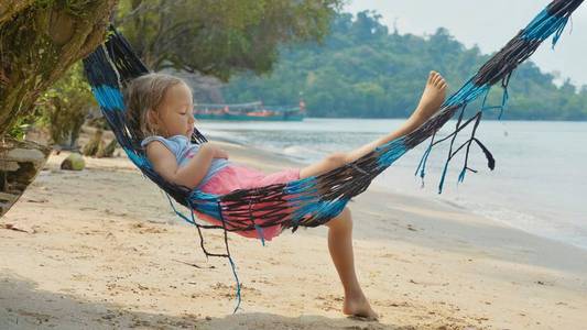 可爱的孩子女孩躺在吊床上, 在沙滩上放松