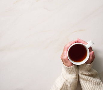 冬日早餐女子捧着一杯热茶, 在石米色大理石桌上, 手里的特写照片带着