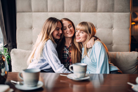 三快乐的女性朋友在咖啡馆里喝咖啡和拥抱