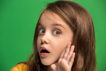 年轻的少女在她的手背后耳语一个秘密绿色背景