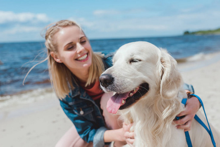 坐在海边的金色猎犬狗的快乐迷人的女人