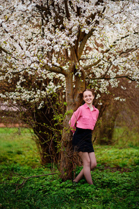 年轻漂亮的女孩在粉红色的衬衫站在盛开的苹果树下, 享受阳光明媚的一天。盛开的春天