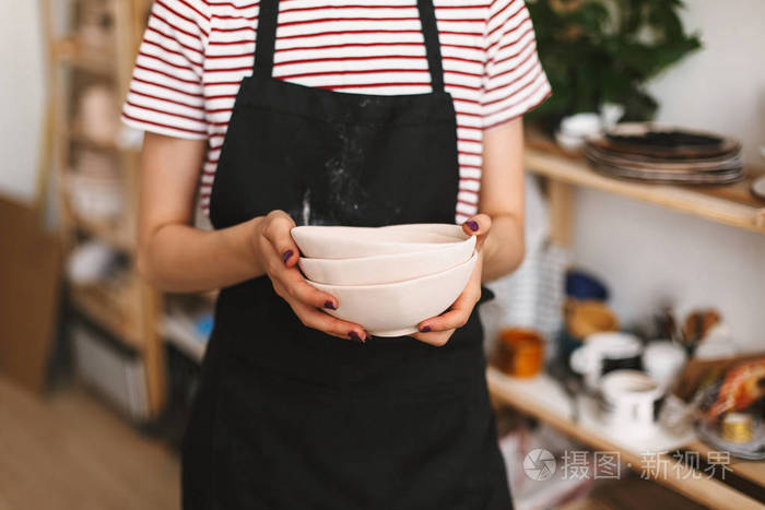 关闭的女孩手持手工碗手上的黑色围裙在陶器工作室
