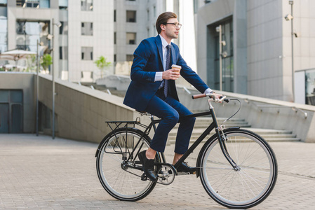 年轻的商人在时髦的西装与咖啡去坐在老式自行车