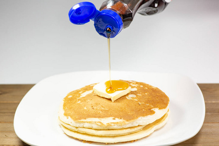 将糖浆从蓝色的尖瓶子倒入黄油的上, 等待被吃掉的金煎饼