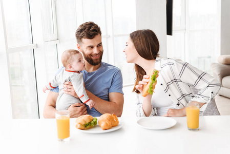 照片可爱有趣的年轻夫妇的父母与他们的小宝贝儿子在厨房吃早餐