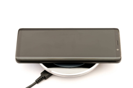现代黑色智能手机充电无线充电器垫。在白色背景上被隔离