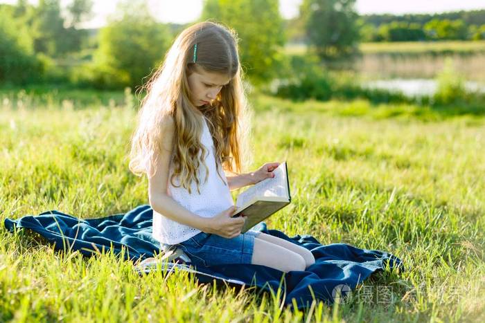8岁的女孩在绿色草地上的肖像.儿童读书, 背景日落田园风光