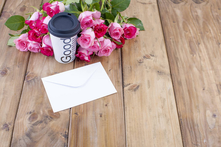 一束新鲜的粉红色玫瑰在一张木桌上。邮件位于白色信封中。文本或明信片的可用空间