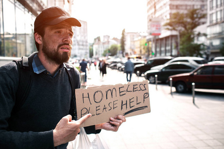 那家伙站在街上, 指着一块纸板, 上面说无家可归的人请帮忙。那家伙在乞求钱和帮助。他绝望了