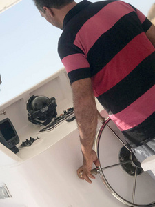 一个黝黑的上尉, 一个穿着红色条纹衬衣的阿拉伯人, 在海上操纵一艘船, 一艘船掌舵。