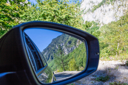 汽车侧面镜子的特写反映了道路上美丽的绿色风景森林