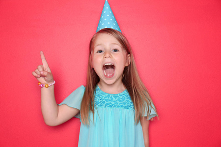 可爱的小女孩与生日帽子和上升的食指在颜色背景