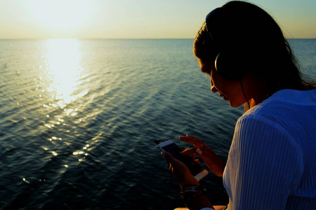 年轻漂亮的女孩听耳机在海边沙滩上的 musicradio