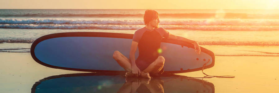 冲浪人的剪影坐与冲浪板在海滨海滩在日落时间