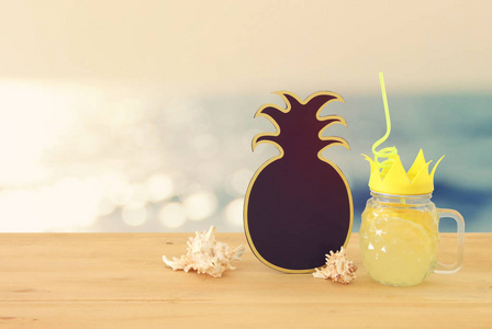 新鲜柠檬水饮料在可爱的菠萝形状玻璃与扭曲的稻草旁边的空黑板在木桌上