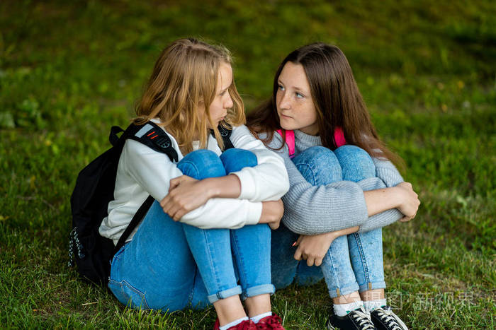 夏天在公园里.他们坐在草地上.与朋友交流的概念.背包后面.