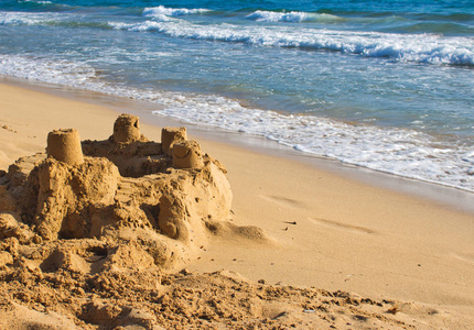沙子城堡在一个阳光明媚的金黄沙滩在地中海与蓝色海和冲浪在背景照片