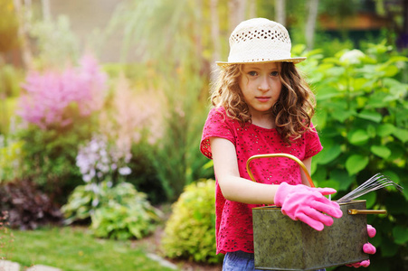 女孩玩小园丁, 并帮助在夏季花园, 戴着帽子和手套, 使用工具