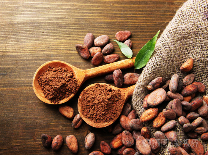 在勺子和木制背景上的可可豆可可粉