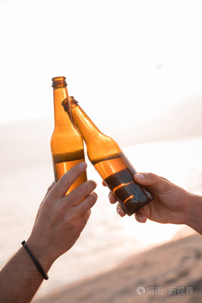 干杯!在海滩上, 手里拿着瓶啤酒举杯祝酒.庆祝概念照片-正版商用图片0