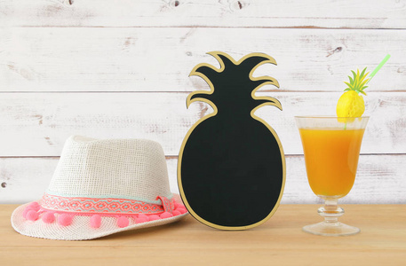 热带和异国水果的图像 coctail, 空白的菠萝黑板在白色软呢帽帽子旁边在木桌上的拷贝空间