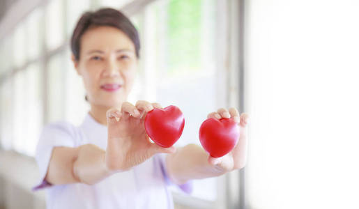 红心抱着微笑的女护士的手, 代表着付出努力的高品质服务精神耐心。专业, 专家在白色一致的概念