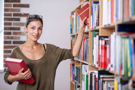 戴眼镜的年轻女子从图书馆书架上拿一本书