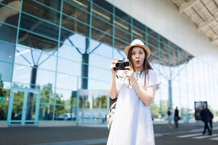 年轻震惊的旅行妇女在帽子与背包举行复古复古照片相机在国际机场。在周末外出旅行的女乘客。航空飞行概念