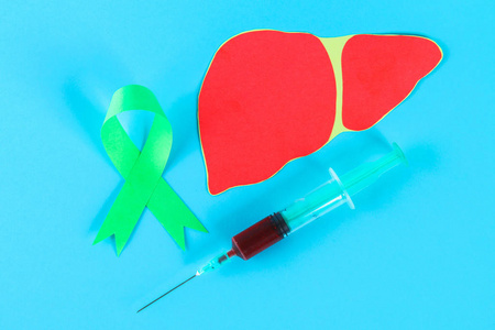 世界肝炎日。6月28日。一条绿色的玉丝带, 一个蓝色的桌子上有血和肝脏的注射器