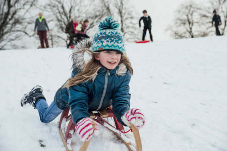 推肚子小女孩躺在她的肚子, 因为她在雪地上的雪橇上下山照片