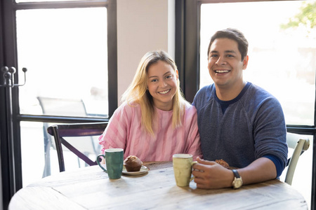 有吸引力和快乐的年轻夫妇的肖像坐在一起在餐馆餐桌上的咖啡和微笑