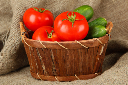 美味的绿色黄瓜和红番茄在篮子里，麻布背景上